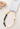 A beaded keychain with white heart-shaped beads, dark green polished beads, light green marbled beads, and gold-toned metal hardware, displayed on a cream ceramic stand.